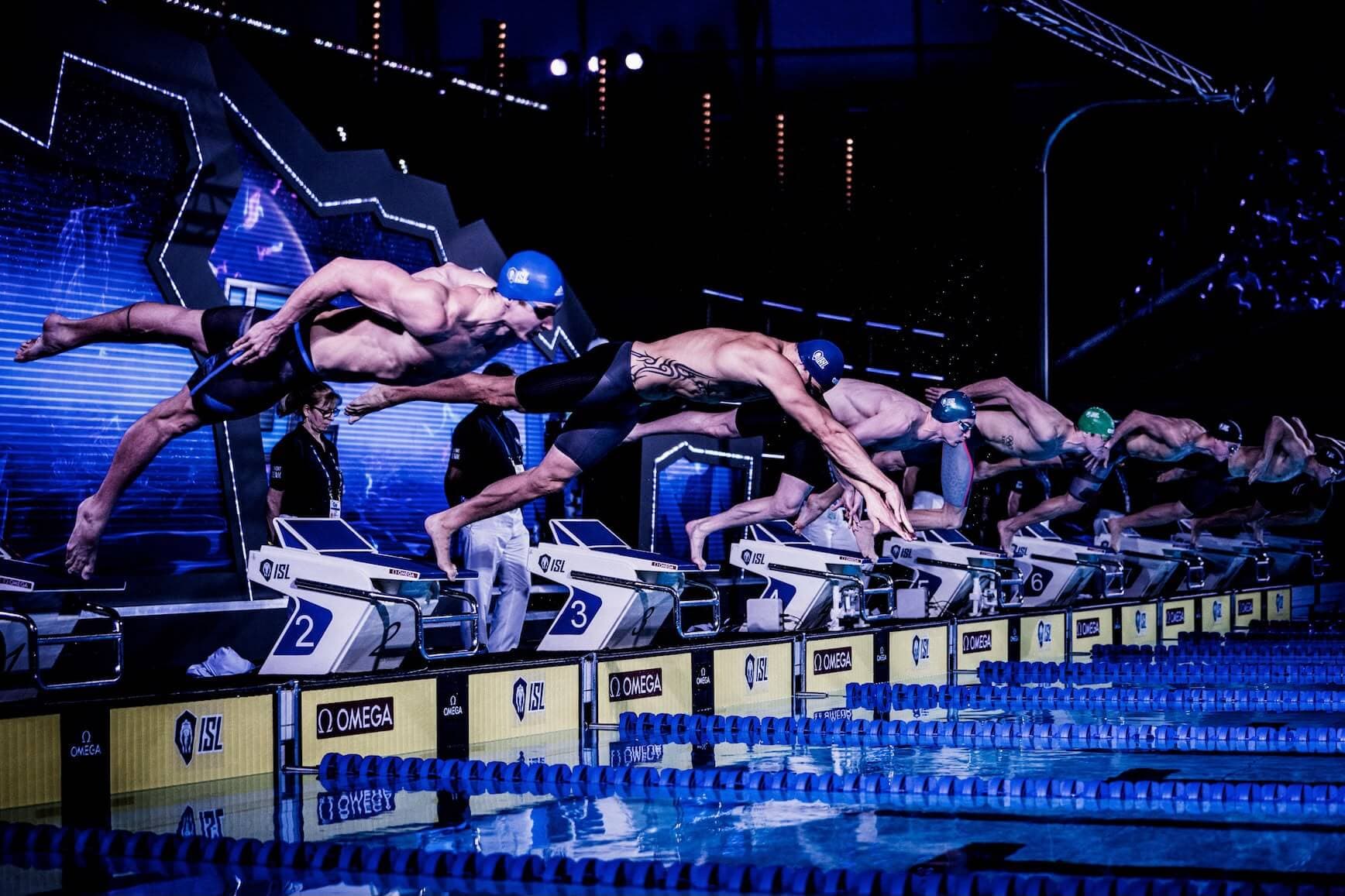 ISL swimmers diving from the starting blocks during a team race